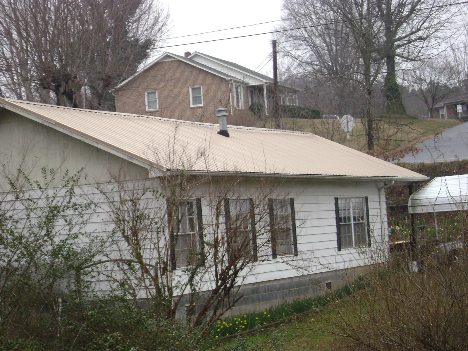 Tan metal roof on a white sided house set into a hillside — Commercial Roofing by Roofing Brothers in Tonopah